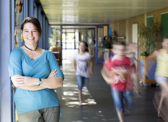Lächelnde Lehrerin in Ihrer Schule mit rennenden Kindern im Gang