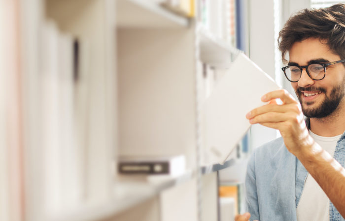 junger Mann mit Buch vor einem Bücherregal