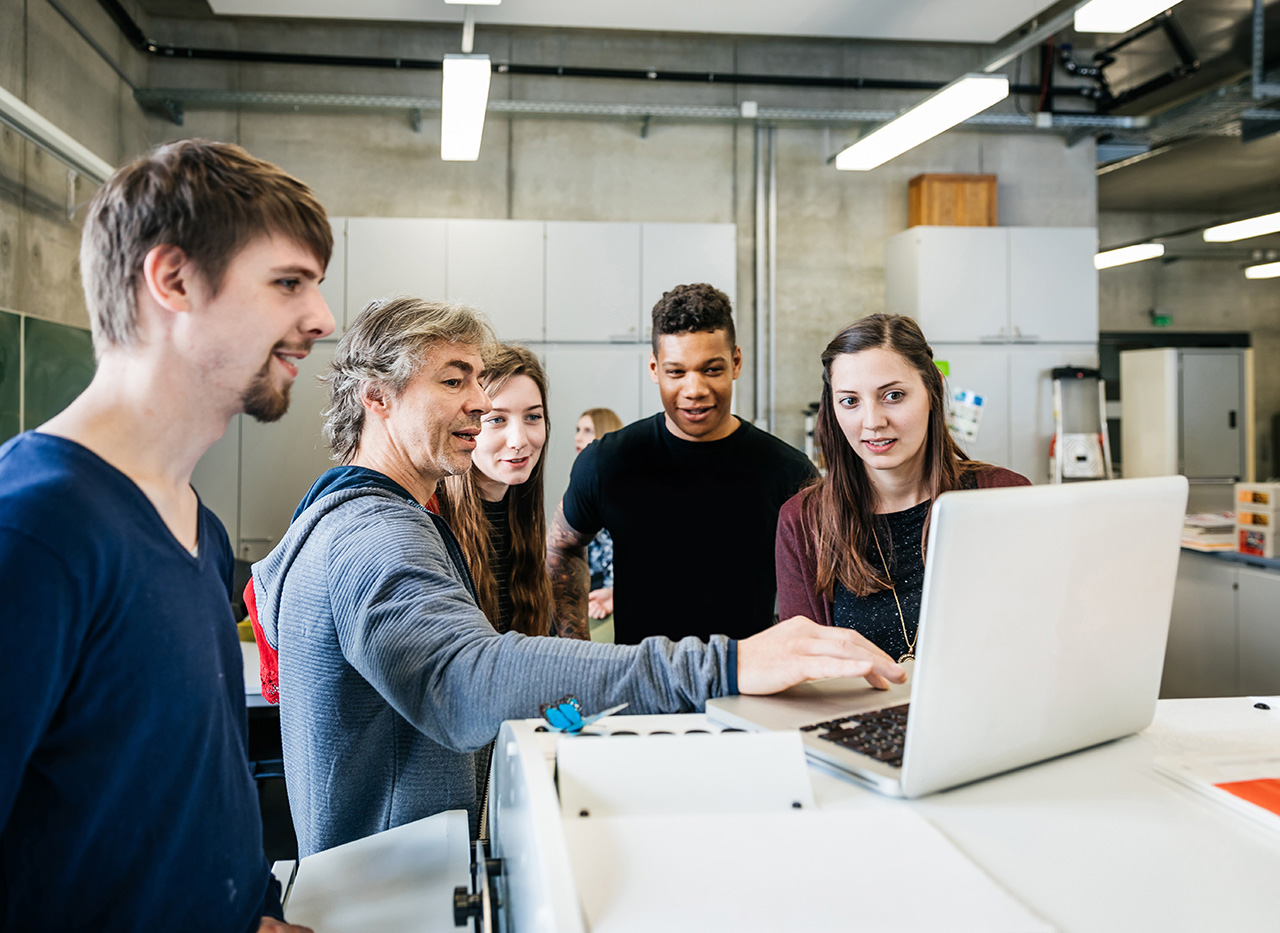 Lehrer erklärt seinen Schülern etwas am Laptop
