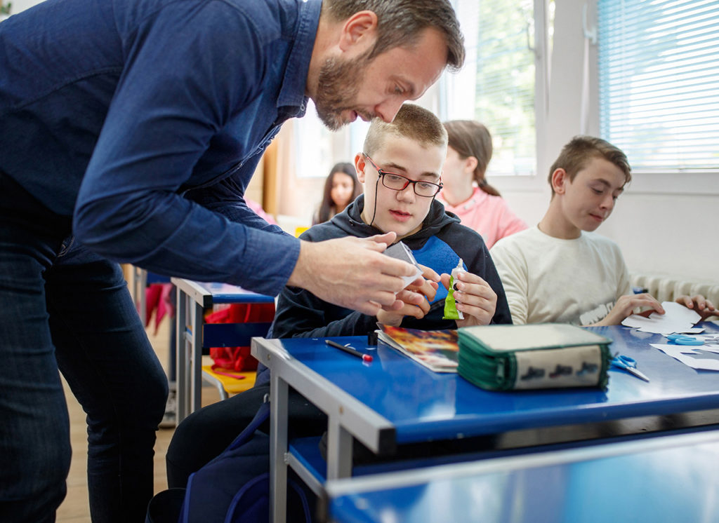 Lehrer erklärt seinem Schüler etwas beim Basteln am Tisch