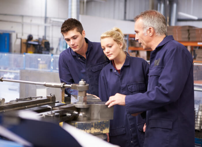 Schüler im Praktikum bei Unternehmen. Ausbilder erläutert Schülerpraktikanten die Funktion einer Maschine in der Werkhalle.