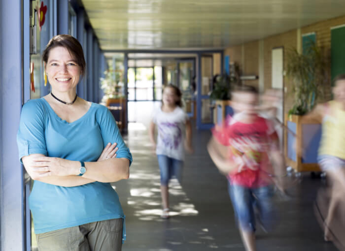 lächelnde Lehrerin steht nach erfolgreicher Unterrichtseinheit zu Berufsorientierung im Flur, in dem Schüler rennen.