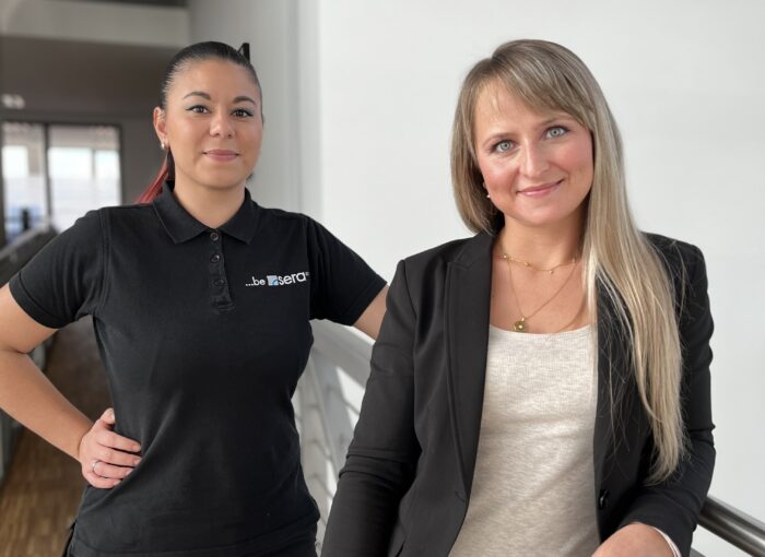 SCHULEWIRTSCHAFT Preisträger sera GmbH - zwei junge Frauen, eine trägt dunklen Blusson, die andere ein Polo-Shirt von sera